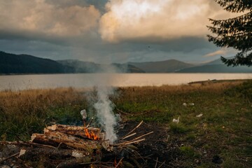Small campfire with gentle flames beside a lake during a glowing sunset