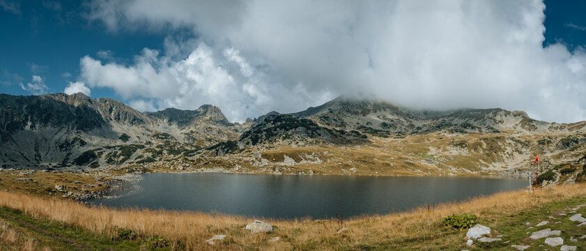 Panoramic shot of a lake surrounded by hills under a cloudy sky