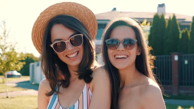Two young beautiful smiling hipster women posing in the street. Sexy trendy models in summer swimwear bathing suits. Positive female. Cheerful and happy outdoors at summer sunny day. In sunglasses