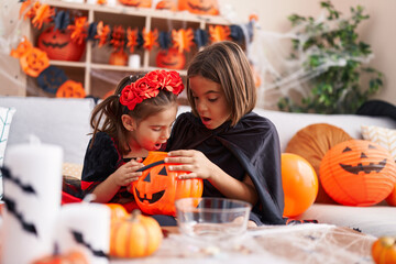 Adorable boy and girl wearing halloween costume looking on pumpkin basket at home