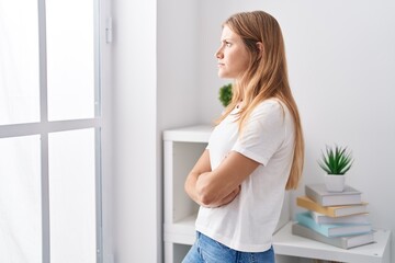 Young blonde girl standing with arms crossed gesture and serious expression at home