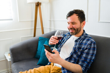 Smiling man enjoying a glass of wine and texting