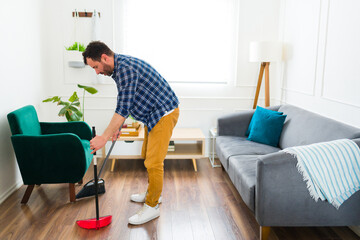Caucasian man sweeping the floor with a broom at home