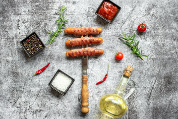 Fototapeta na wymiar sausages wrapped in bacon grilled on a meat fork on a stone background