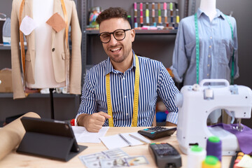 Hispanic man with beard dressmaker designer working at atelier winking looking at the camera with...