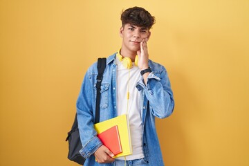 Hispanic teenager wearing student backpack and holding books touching mouth with hand with painful...