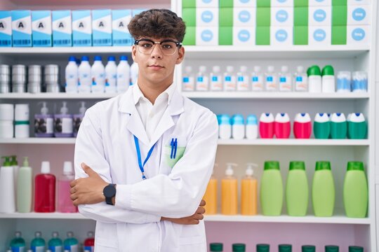 Young hispanic teenager pharmacist smiling confident standing with arms crossed gesture at pharmacy