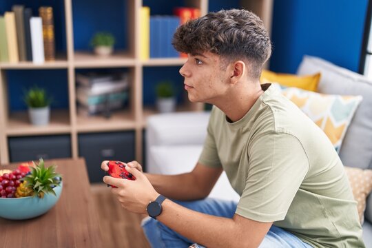 Young hispanic teenager playing video game sitting on sofa at home