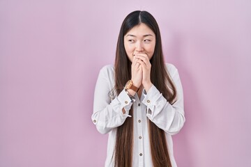 Chinese young woman standing over pink background laughing nervous and excited with hands on chin looking to the side