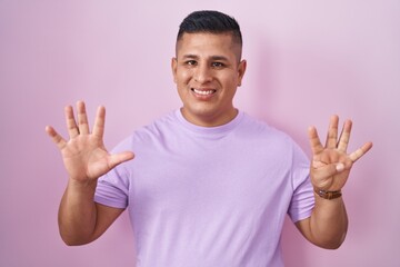 Young hispanic man standing over pink background showing and pointing up with fingers number nine...