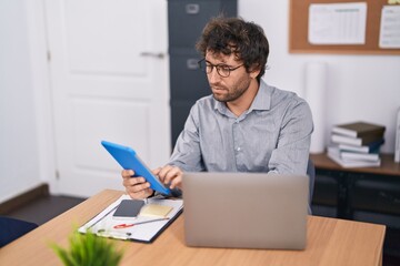 Fototapeta premium Young hispanic man business worker using touchpad and laptop at office