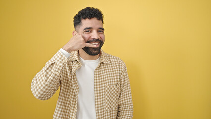 Young hispanic man smiling confident doing call me gesture with hand over isolated yellow background