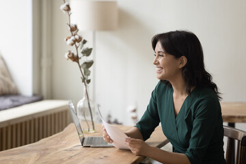 Happy businesswoman sit at desk in homeoffice with documents, smile, get good news in paper notice letter, bank statement, receive job offer, look through financial report feels satisfied. Good result