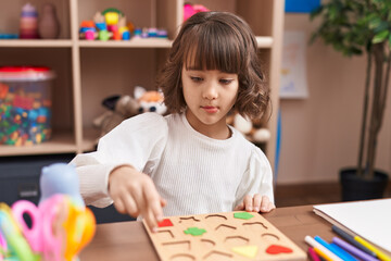 Adorable hispanic girl playing with maths puzzle game sitting on table at kindergarten