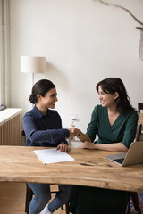Obraz premium Two young multiethnic women, office workers shake hands in modern office after successful work or job interview, satisfied with cooperation, making good deal, sign contract, starting or finish meeting