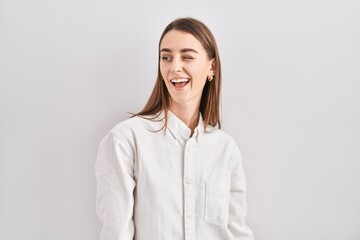 Young caucasian woman standing over isolated background winking looking at the camera with sexy expression, cheerful and happy face.