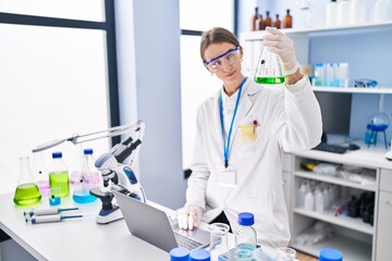 Young caucasian woman scientist holding test tube using laptop at laboratory