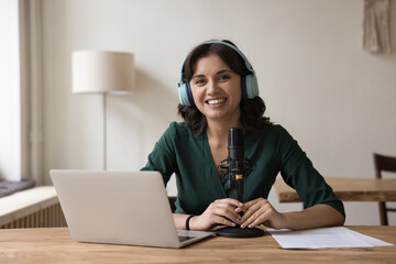 Woman radio host in headphones sit at desk with microphone and laptop, take part in online...