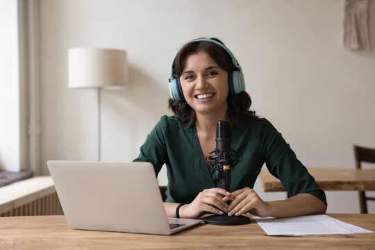 Woman radio host in headphones sit at desk with microphone and laptop, take part in online conference, videocall, look at camera. Portrait of blogger, influencer, streamer, record webinar or podcast