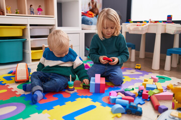 Adorable boy and girl playing with construction blocks sitting on floor at kindergarten