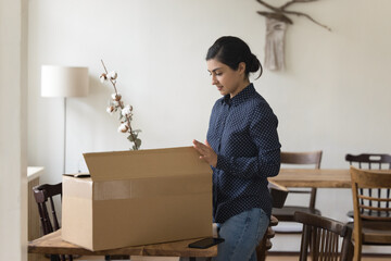 Millennial serious Indian woman get parcel, open box to review received goods. Young businesswoman...