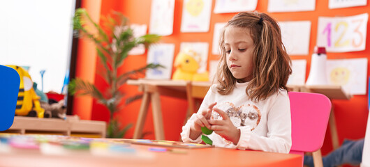 Adorable hispanic girl playing with maths puzzle game sitting on table at kindergarten