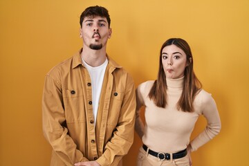 Young hispanic couple standing over yellow background making fish face with lips, crazy and comical gesture. funny expression.