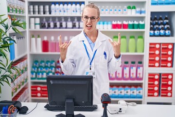 Young caucasian woman working at pharmacy drugstore shouting with crazy expression doing rock symbol with hands up. music star. heavy concept.