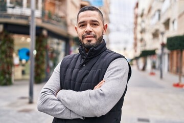 Young latin man standing with arms crossed gesture at street