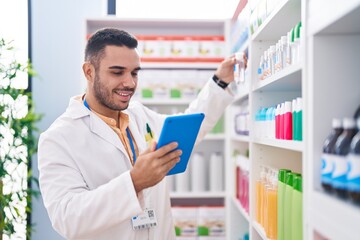 Naklejka na ściany i meble Young hispanic man pharmacist using touchpad working at pharmacy