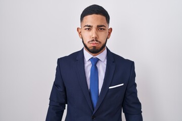 Young hispanic man wearing business suit and tie puffing cheeks with funny face. mouth inflated with air, crazy expression.