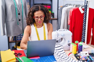Middle age woman tailor smiling confident using laptop at clothing factory