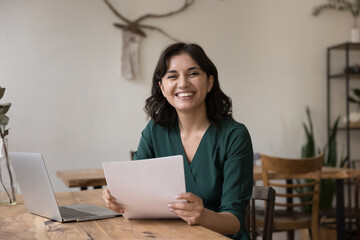 Happy young Armenian business-woman sits at desk with sheets in hands, get documents, legal paper...
