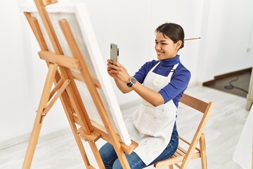 Young latin woman smiling confident make photo to draw canvas at art studio