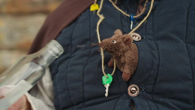 Sorcerer shows mouse elixir in glass bottle. Animal sniffs liquid sitting in bosom. Knight with magical abilities chats with toy animal closeup on blurred background