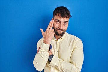 Handsome hispanic man standing over blue background shooting and killing oneself pointing hand and fingers to head like gun, suicide gesture.