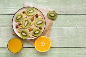 Bowl with tasty oatmeal, nuts, orange, kiwi and glass of juice on green wooden background