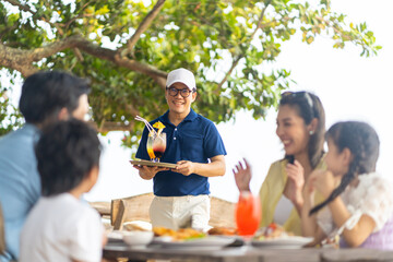 Happy Asian family couple and little kids travel ocean on summer holiday vacation. Waiter serving...