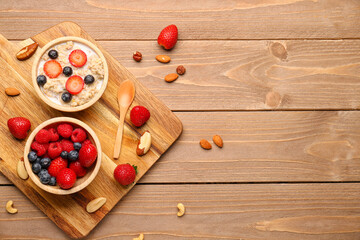 Bowls with tasty oatmeal, ripe berries and nuts on wooden background