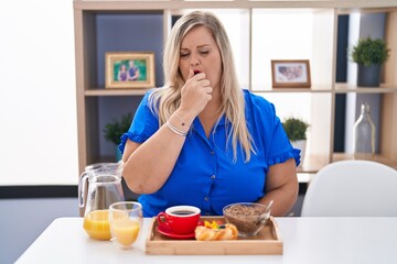 Caucasian plus size woman eating breakfast at home feeling unwell and coughing as symptom for cold or bronchitis. health care concept.