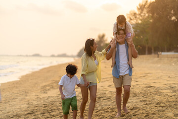 Happy Asian family travel ocean on summer holiday vacation. Parents and children kid enjoy and fun outdoor activity lifestyle walking and playing together at tropical island beach at summer sunset.