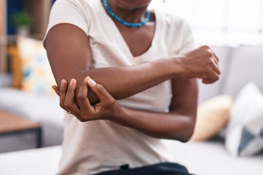Middle age african american woman sitting on sofa suffering for elbow pain at home