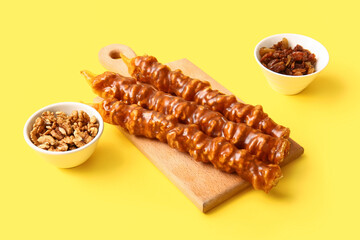 Wooden board with tasty churchkhela, raisin and walnuts on yellow background