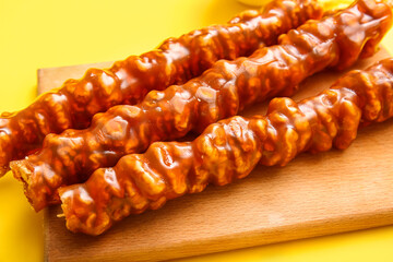 Wooden board with tasty churchkhela on yellow background, closeup