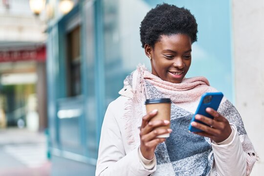 African american woman using smartphone drinking coffee at street