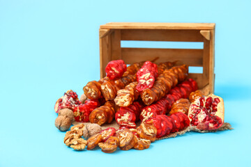 Overturned box with delicious churchkhela and walnuts on blue background