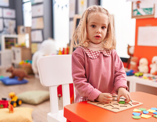 Adorable blonde girl playing with maths puzzle game at kindergarten