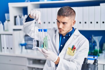 Young hispanic man scientist holding test tubes at laboratory