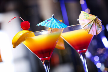 Glasses of tasty Tequila Sunrise with umbrellas against blurred background, closeup