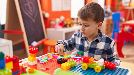 Adorable caucasian boy playing with construction blocks sitting on table at kindergarten